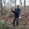 Man stood in woodland in winter tying together a bundle of poles