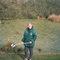 Woman in green coat smiling at camera stood in front of a large pond holding a pond dipping net.