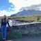 Woman with blond hair stood by a wall with view of mountains beyond