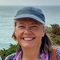 Headshot of a woman smiling wearing a blue cap with ocean visible in background