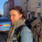 Woman with dark hair wearing scarf and backpack looking at camera