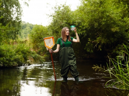 Girl standing in river in waders with net and jar