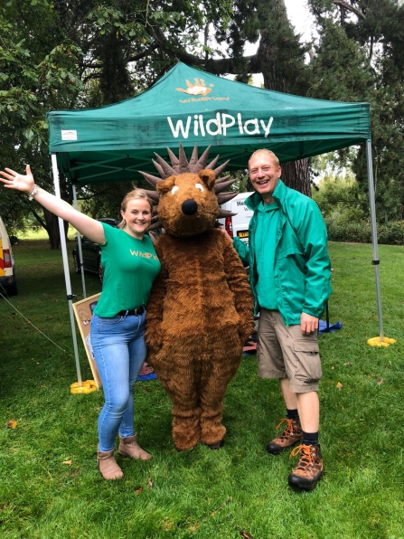 A man and a woman standing either side of a person in a hedgehog costume!