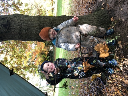 Two toddlers holding twig and leaf crafts, smiling.