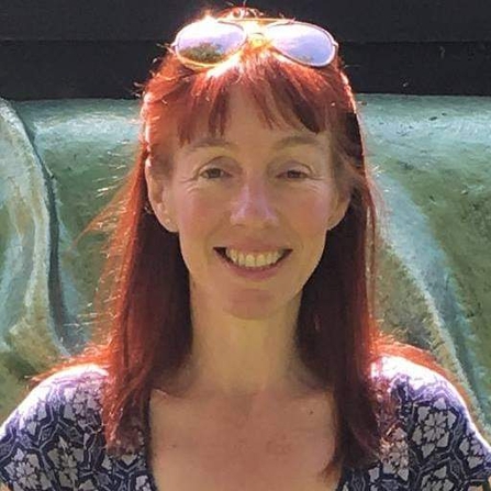 Head shot of woman with long red hair and sunglasses on her head smiling at camera