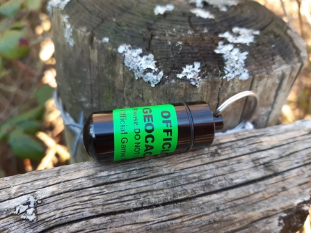 Small black phial with green sticker around on top of a fence