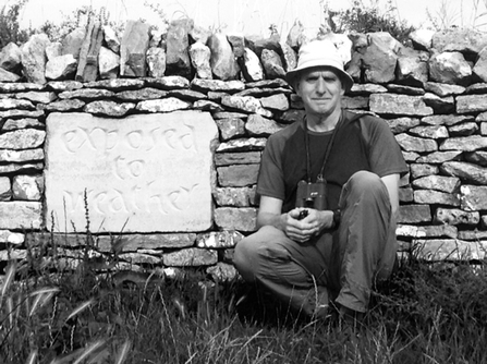 Man crouched by a dry stone wall looking at camera