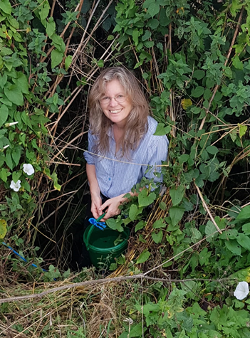 Woman with long hair and pale blue shirt surrounded by vegetation