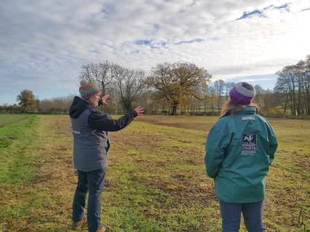 Two women in coats and hats in a field with trees in the background