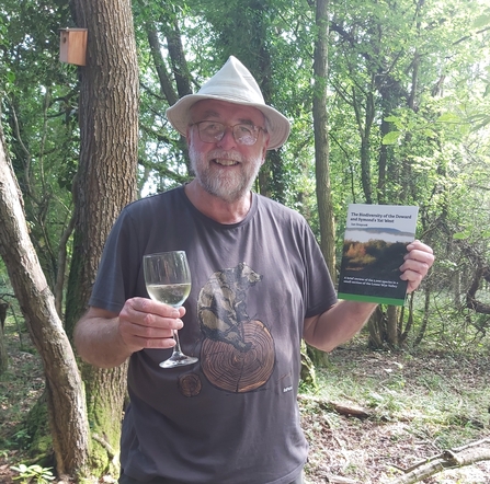 Man holding book in one hand and wine glass in the other, smiling at camera