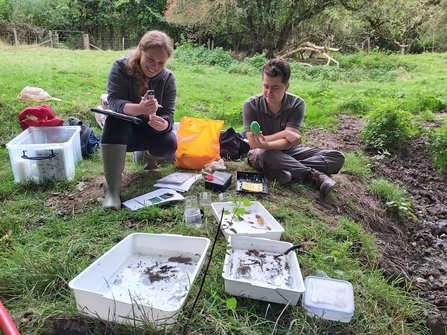 A man and woman sat on a bank with white trays and equipment