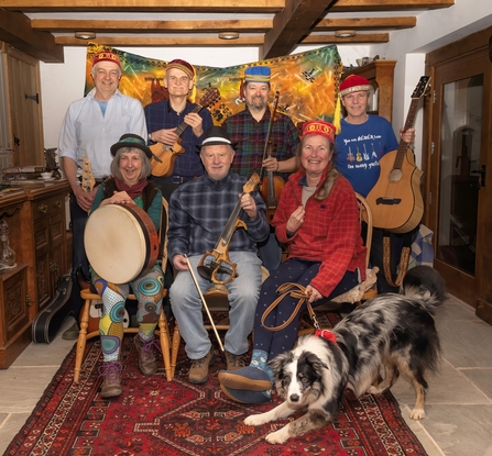 Seven people, some with instruments, stood and sat for photo with dog at the front.