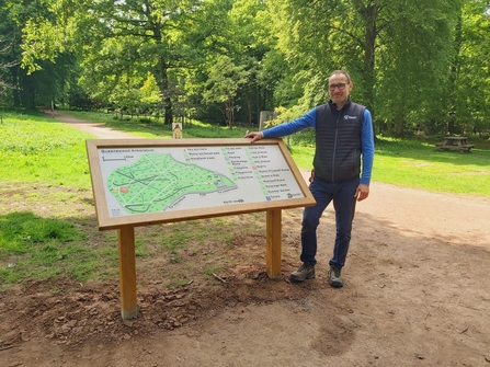 Man stood beside large angled interpretation sign board in woodland
