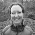 Headshot of woman smiling at camera, hair tied back, wearing an outdoor coat