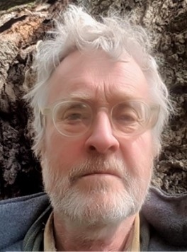 Headshot of a man with grey hair and wearing clear-framed glasses