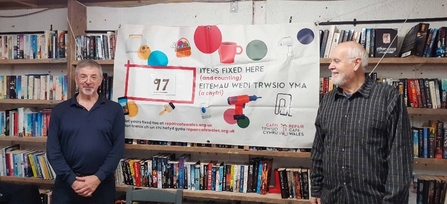 Two men stood either side of a banner in front of a bookshelf