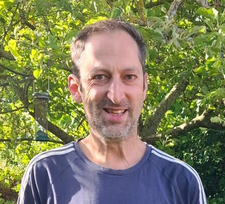 Man with short dark hair and stubble beard in a blue t-shirt, smiling