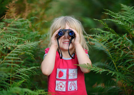 Young girl with blond hair looking through binoculars towards viewer