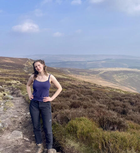 Young woman stood on hilltop path with views across landscape behind