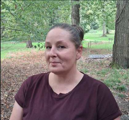 Woman with hair tied back in a maroon t-shirt with woodland in the background