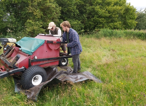 Two men stood behind a red machine in a field