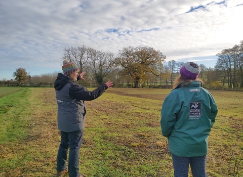 Two women in coats and hats in a field with trees in the background