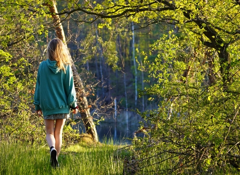 Young woman in green hoodie walking away through sunny woodland